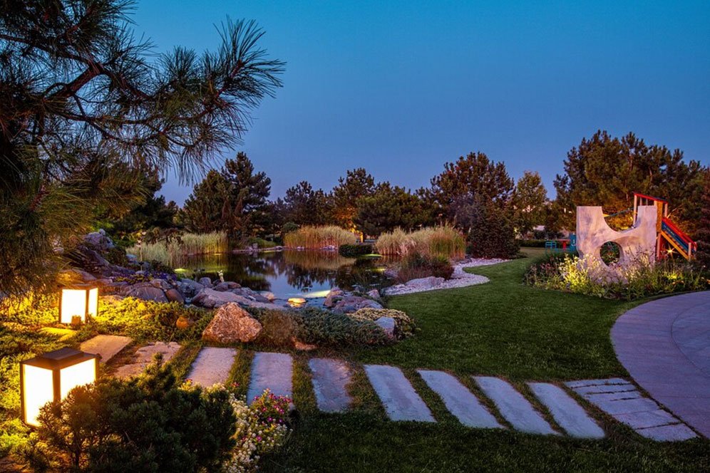 A serene night garden featuring twinkling lights and a tranquil pond reflecting the starry sky.