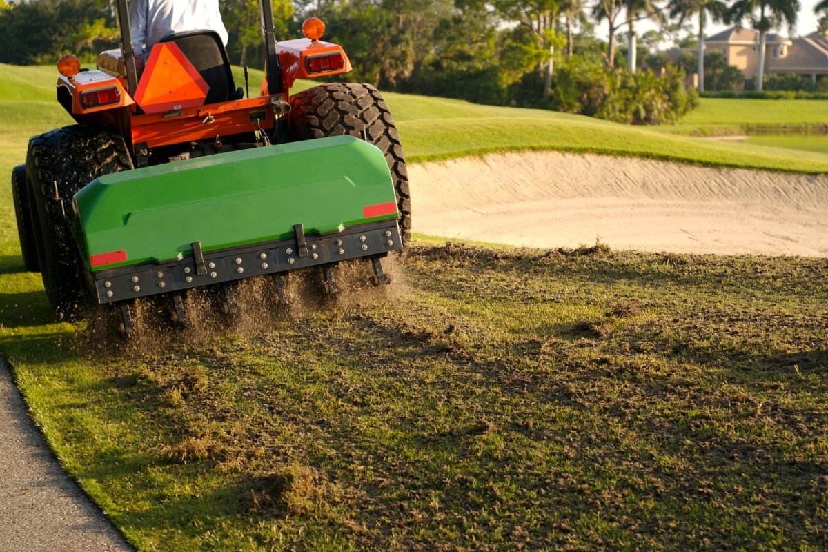A man operates a tractor, efficiently mowing the grass in a lush green field under clear skies.