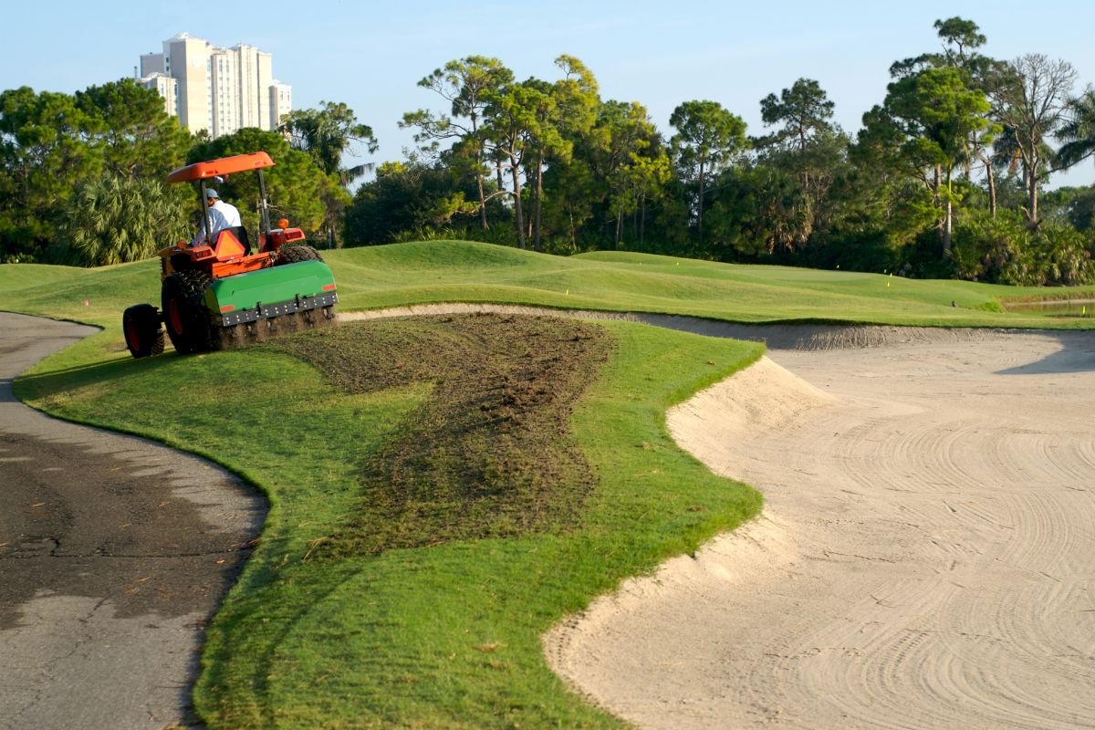 A man meticulously tending to the lush greens of a golf course, showcasing dedication to maintaining the landscape.